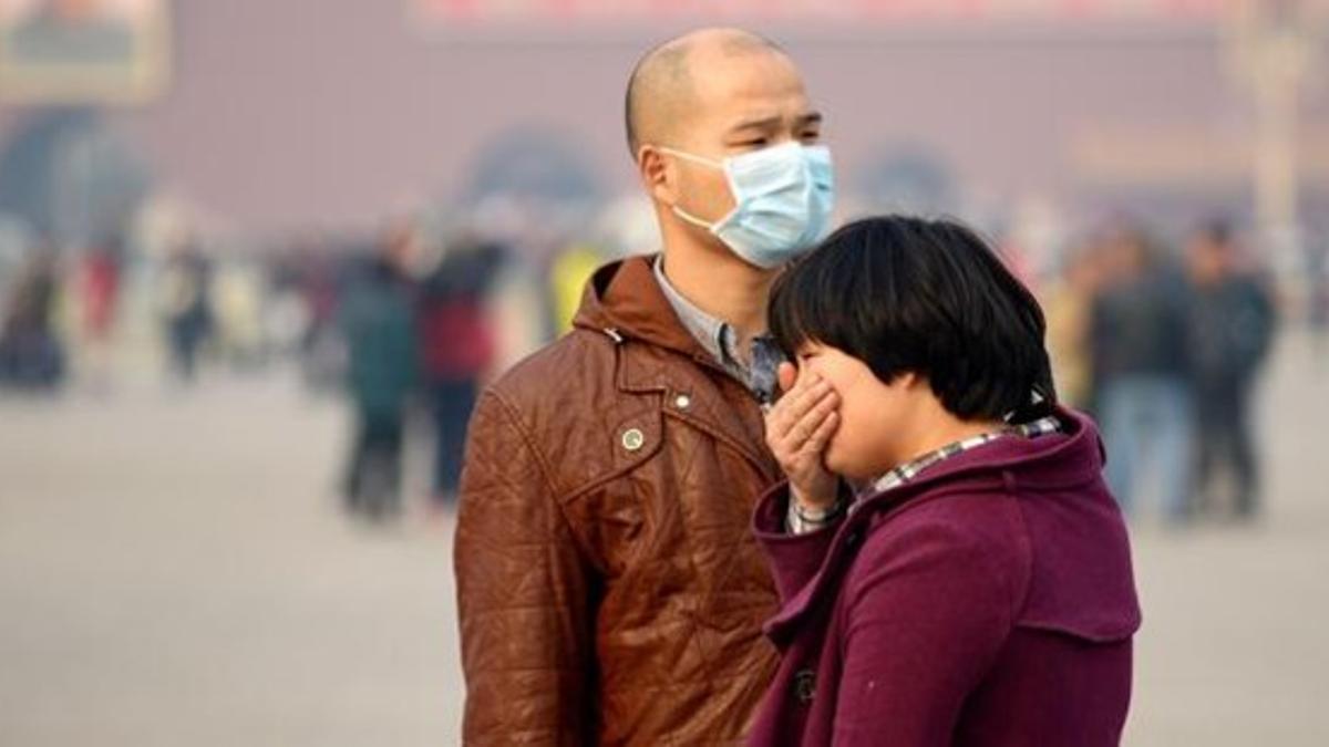 Un hombre usa una máscara y una mujer se tapa con la mano para protegerse de la contaminación en la plaza de Tiananmen, en Pekín, este martes.