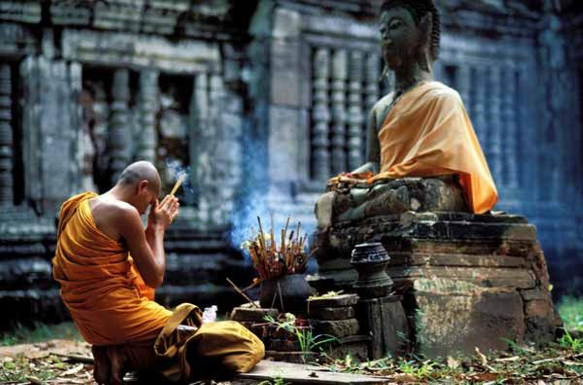 Monje budista rezando frende a la estatua de un buda en el templo de Wat Phu