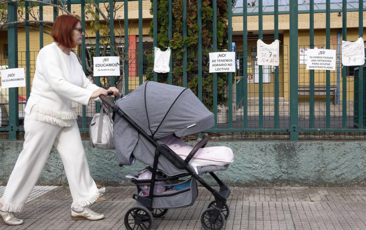 Una mujer pasa con un carricoche por delante de la escuelina de La Magdalena, en Avilés, con carteles de protesta. |  M. L. / Á. G. / R. A. / M. Á. G. / L. P.