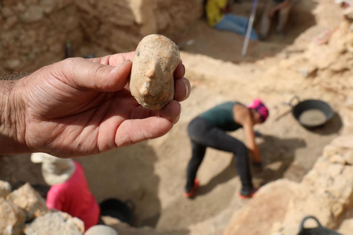 Pla detall del cap femení localitzat durant les excavacions d'Empúries i, al fons, l'excavació de la casa grega