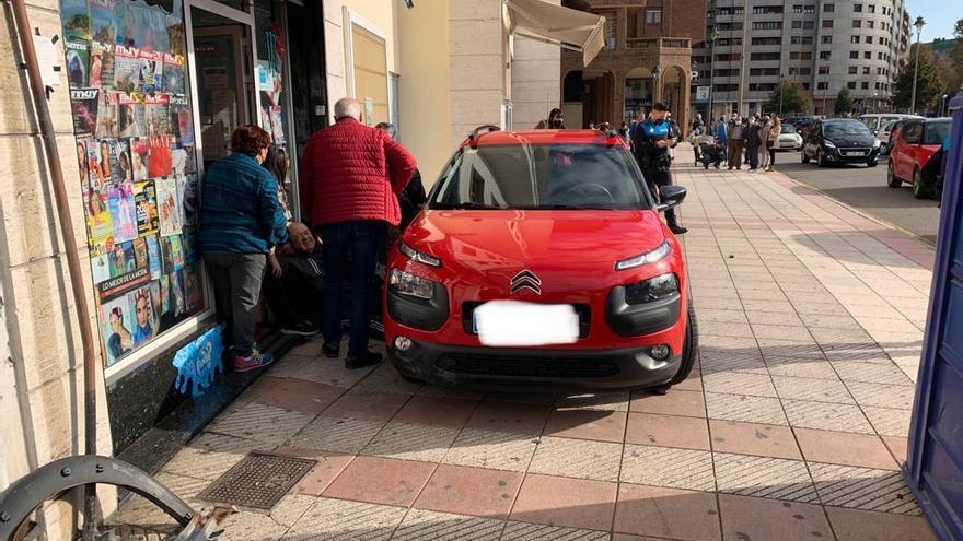 El coche causante del accidente, subido a la acera, y el peatón herido, auxiliado por varios transeúntes.