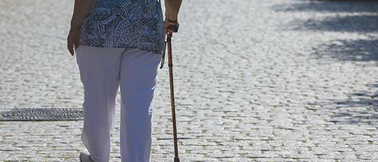 Una persona mayor pasea sola ayudada por un bastón.