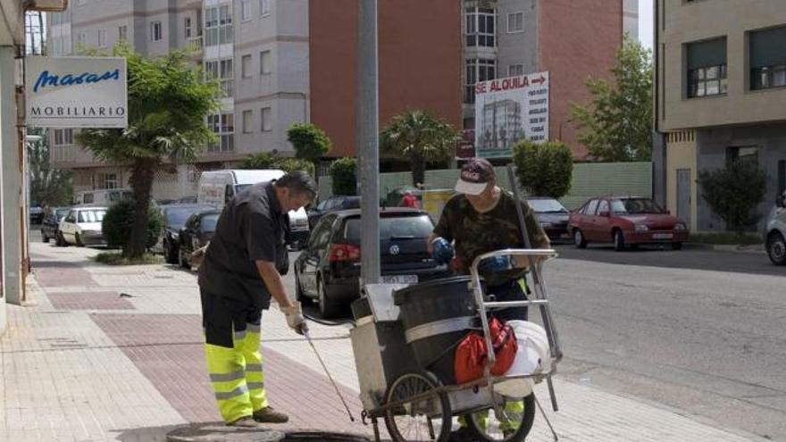 Dos operarios limpian una alcantarilla en El Ferial.