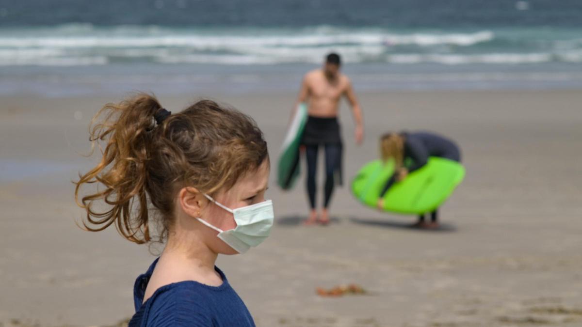 Una niña con mascarilla en la playa