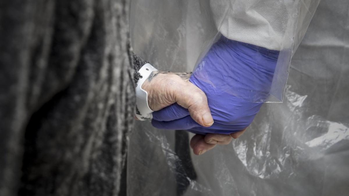 Un sanitario sostiene la mano de una persona mayor.