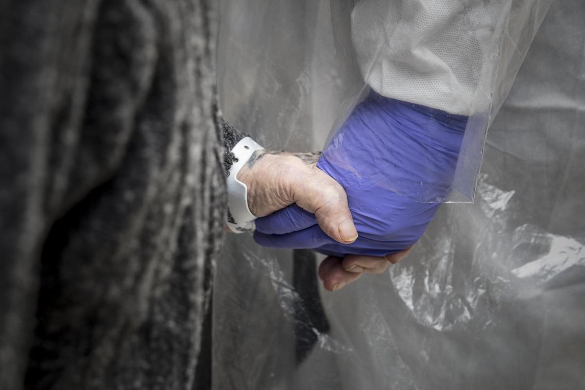 Un sanitario sostiene la mano de una persona mayor.