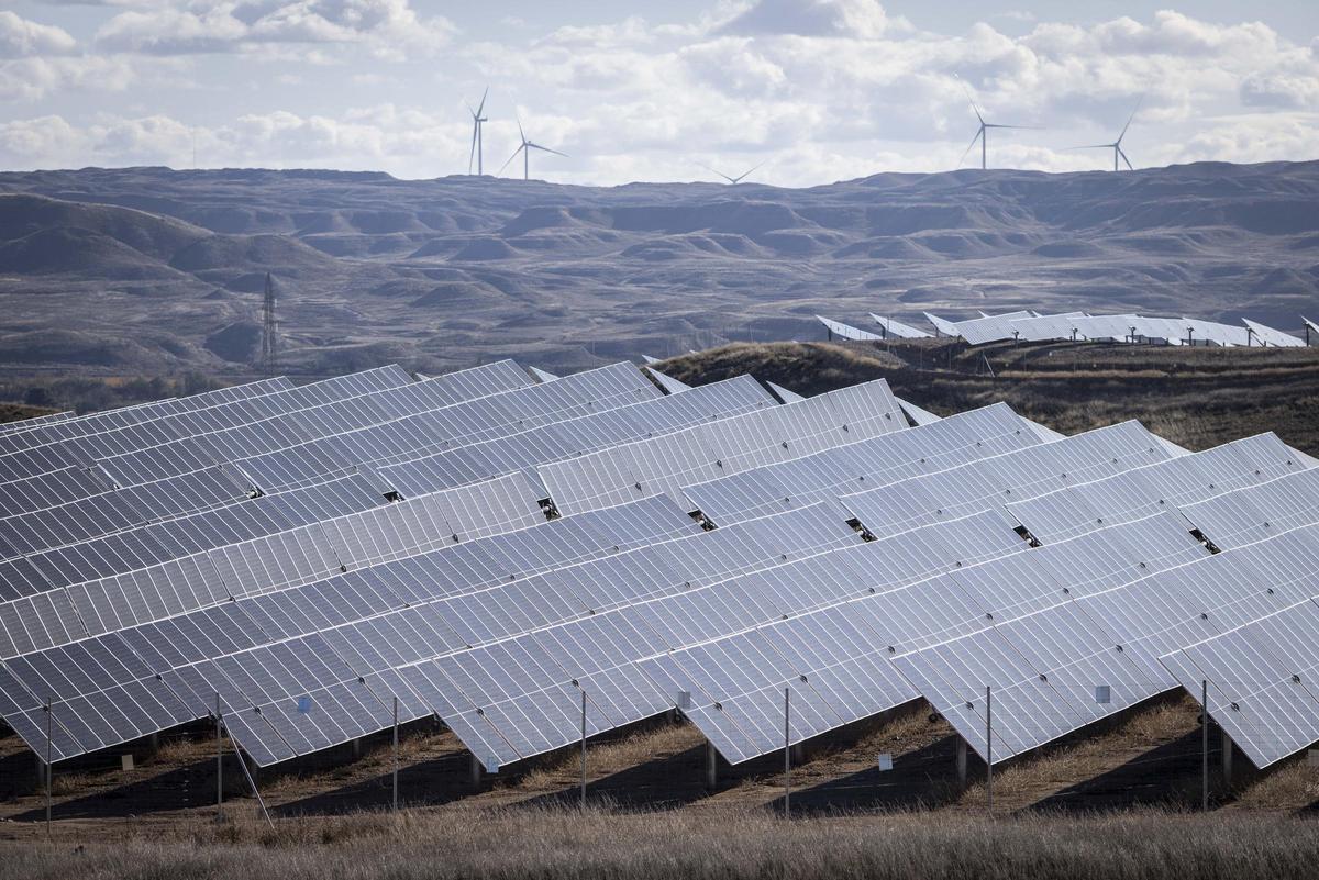 Un parque fotovoltaico de Aragón, con molinos de viento de fondo.