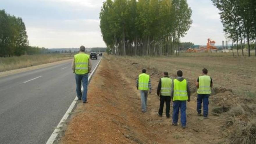 Obreros caminan por el arcen de la carretera donde ha comenzado el movimiento de tierras.