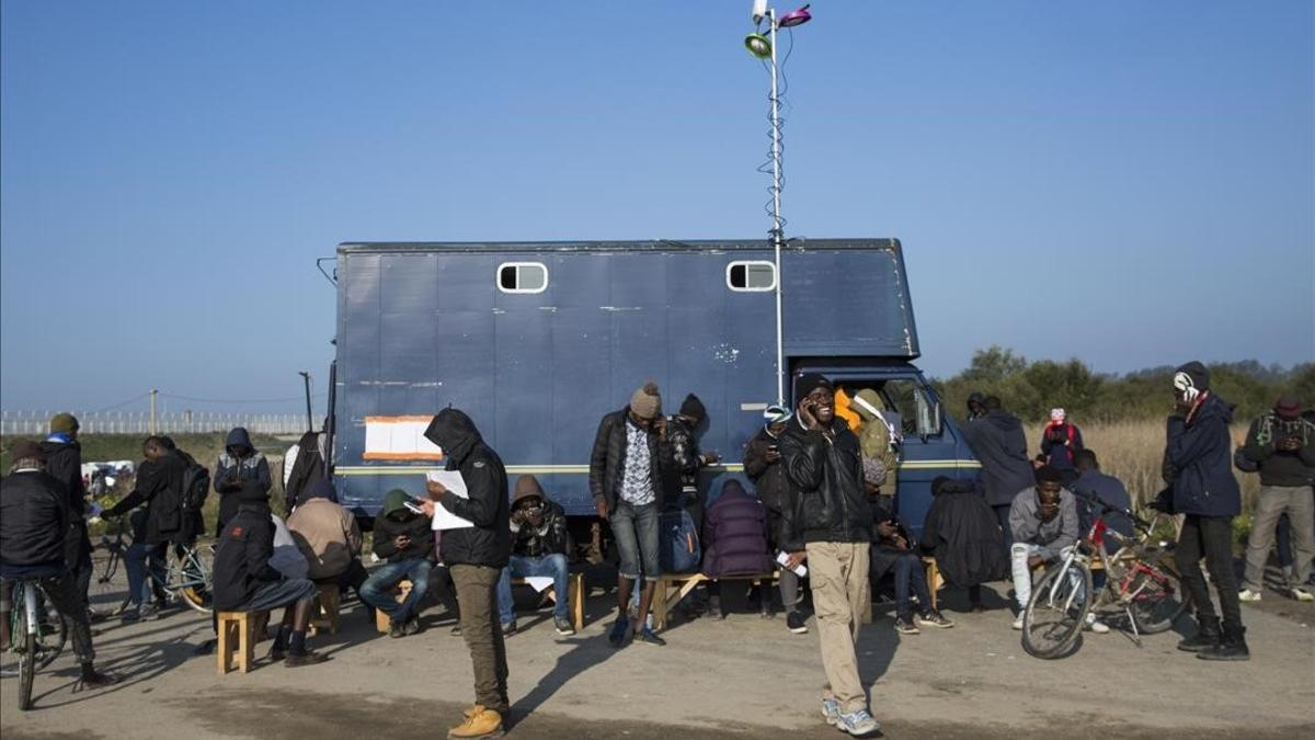 Inmigrantes del campamento francés de Calais usan teléfonos móviles junto a un camión que ofrece conectividad.