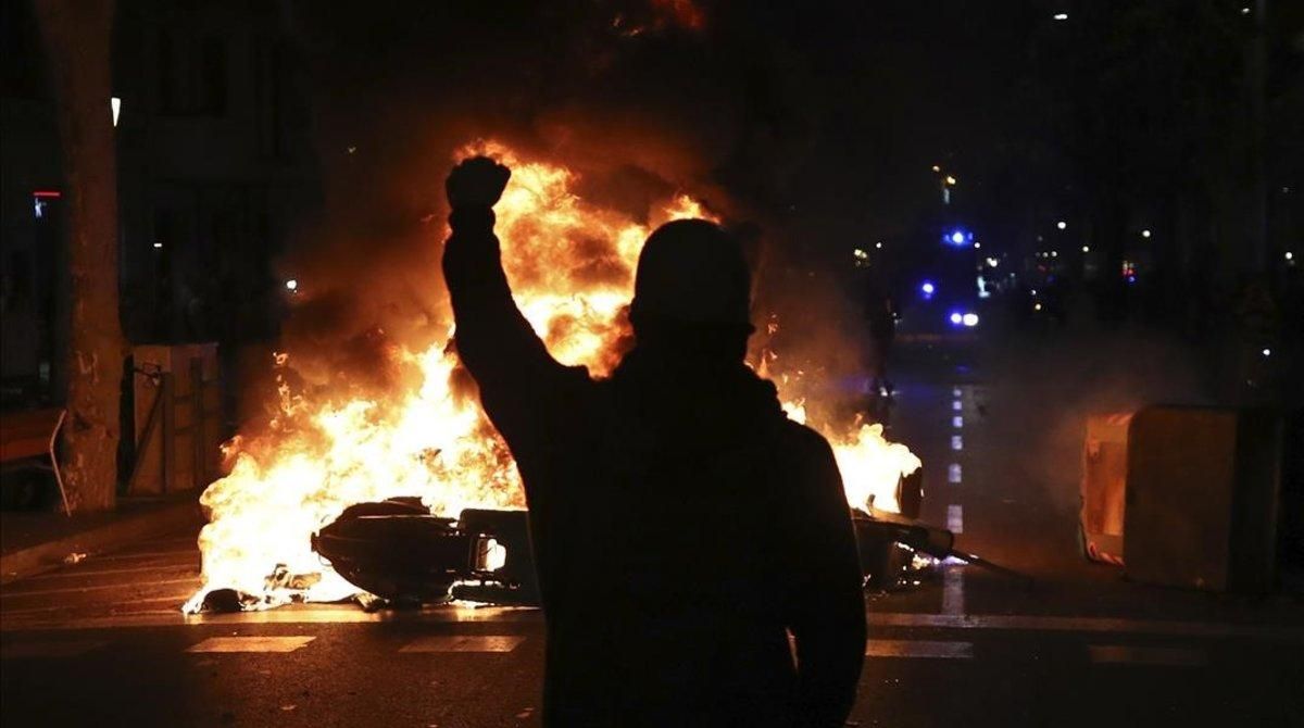 undefined50419990 a protestors raises his fist at police across a burning barr191015234010