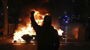 undefined50419990 a protestors raises his fist at police across a burning barr191015234010
