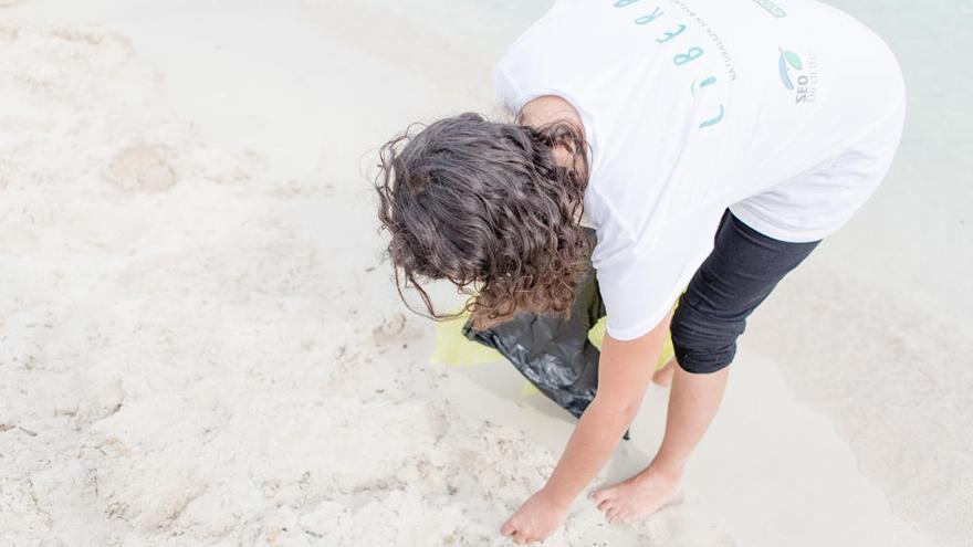 Un niño recoge residuos en la playa.