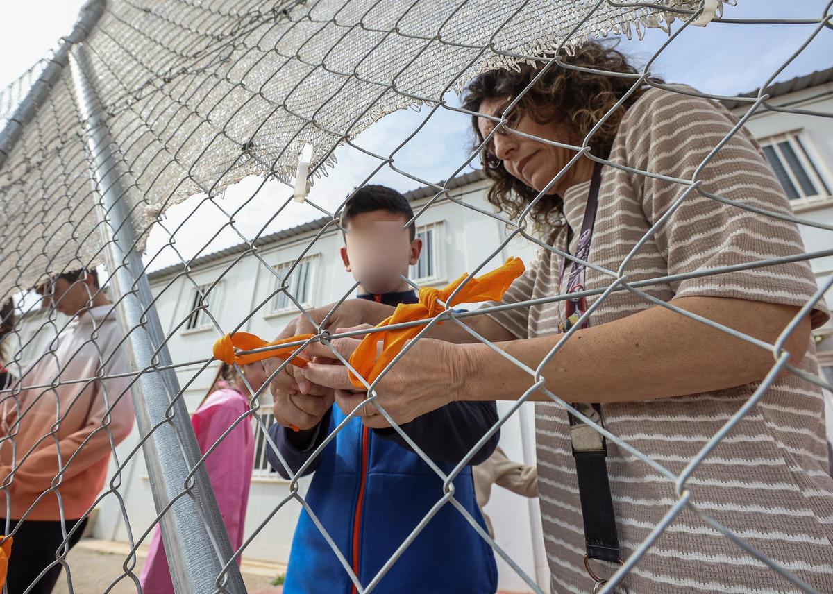Un estudiante de El Somni pone un lazo en la valla del centro junto a una profesora.