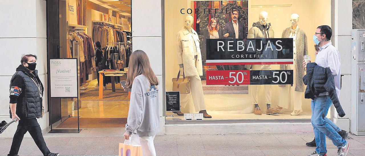 Viandantes pasan frente al escaparate de una tienda de la calle Enmedio de Castelló que ya luce el cartel de rebajas.