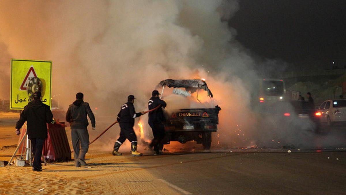 Dos bomberos tratan de apagar un coche incendiado durante los disturbios protagonizados por aficionados al fútbol en El Cairo el pasado 8 de febrero