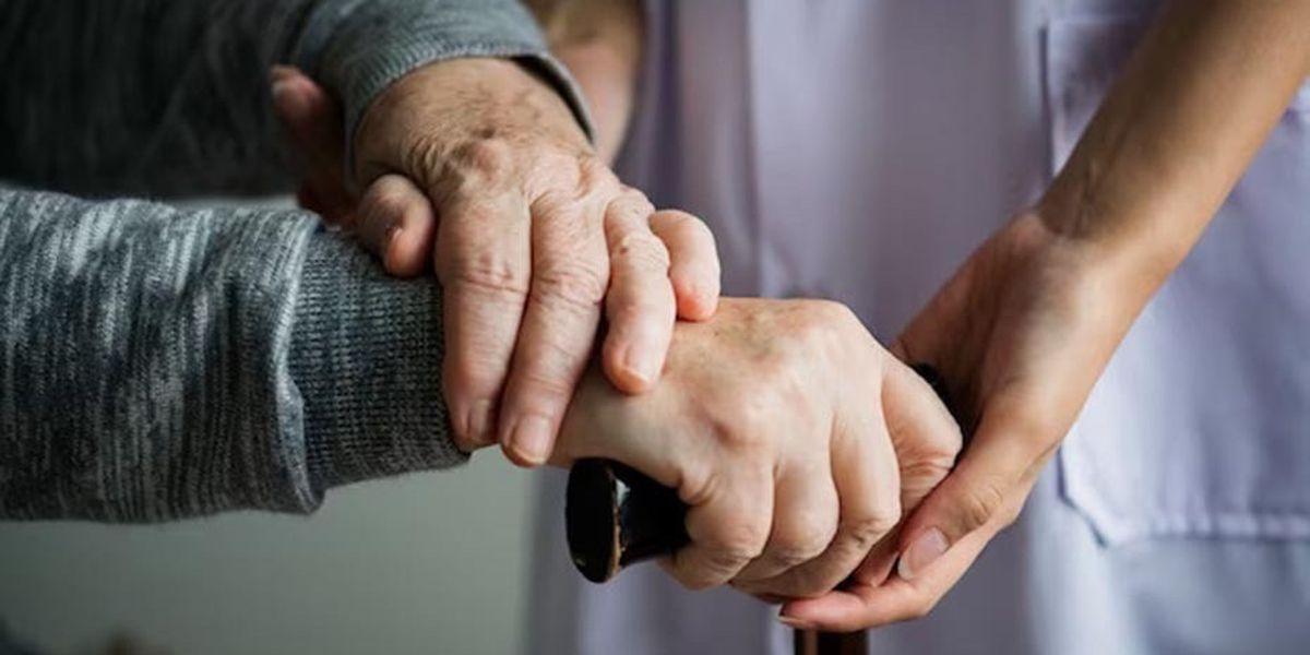 Imatge d'arxiu d'una persona assistent agarrant de la mà a una persona dependent.