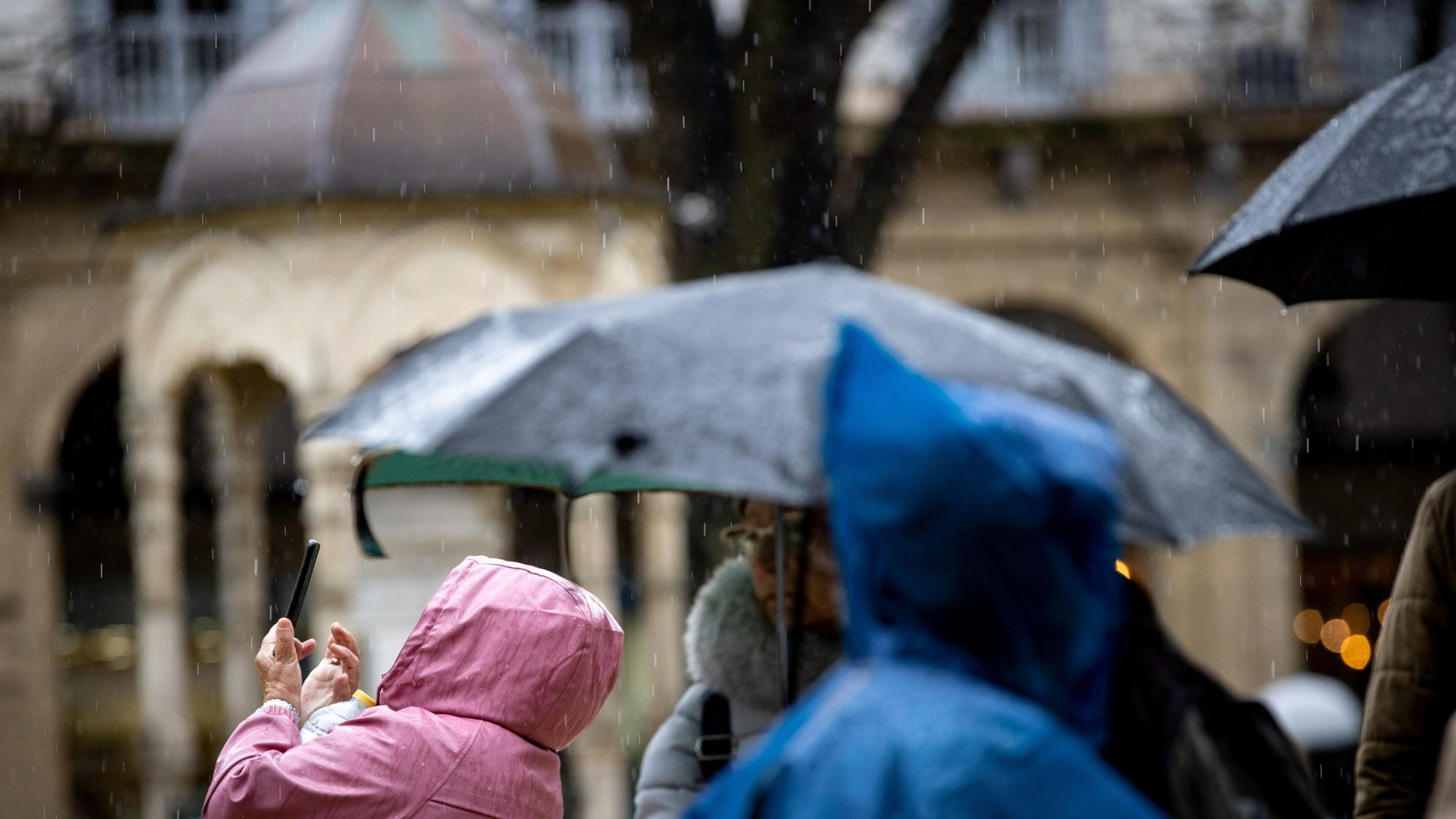 Un grupo de turistas trata de protegerse de la lluvia este jueves en San Sebastián.