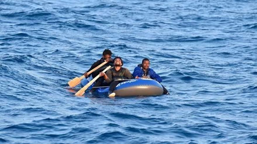 Tres immigrants a bord d&#039;una embarcació pneumàtica, a punt de ser rescatats.