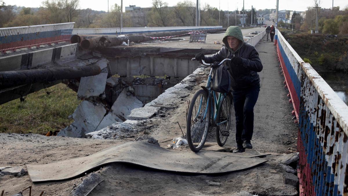 Un residente de Borivske, en la región de Járkov, pasa con su bicicleta sobre un puente destruido por los bombardeos