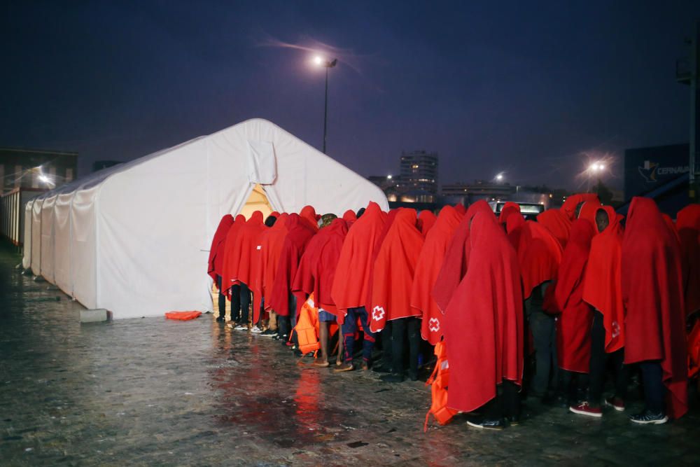 Migrants stand under the rain after disembarking ...