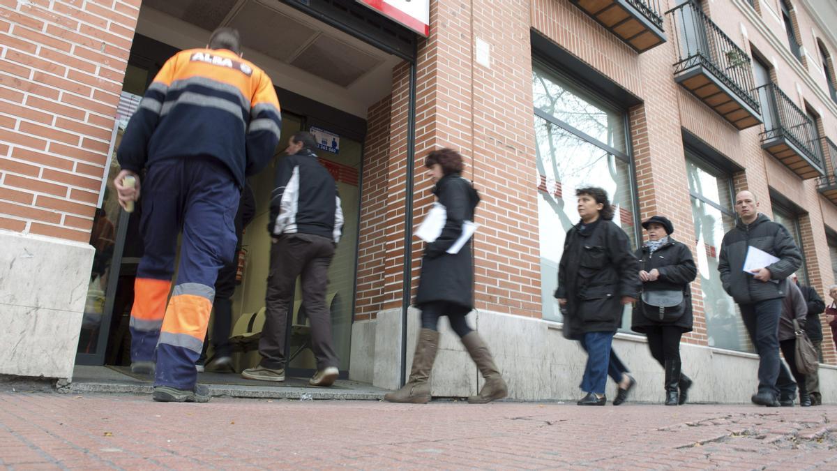 Varias personas, junto a una oficina de empleo.