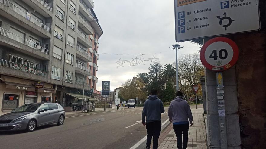 Dos jóvenes, pasando junto a una de las señales que indican las ubicaciones de varios aparcamientos en la villa situada a la entrada de Grado. | S. Arias