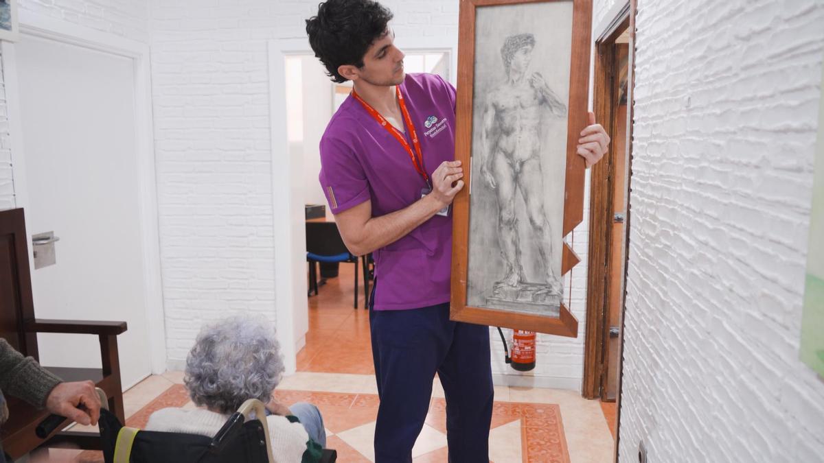 Charo, de espaldas en silla de ruedas, junto a una de sus pinturas.