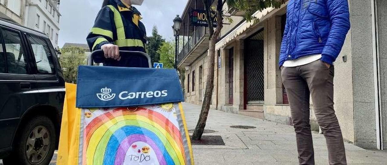 Una cartera de Lalín con mensajes en su carrito conversa con un viandante, ambos equipados con mascarilla. // Bernabé