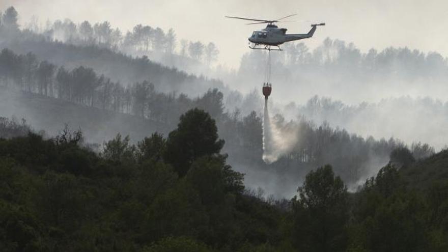 Un helicóptero lanza agua sobre las llamas que asolan el paraje natural de Los Cerros, en Llombai.