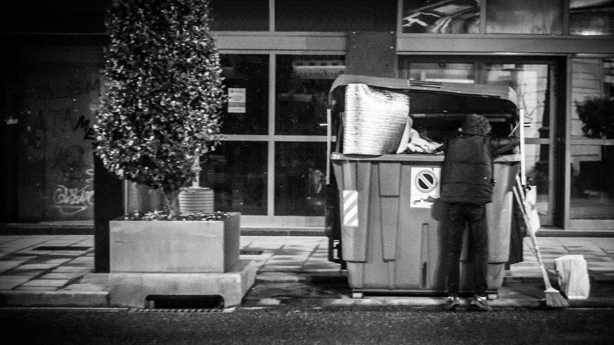 Un hombre rebusca en un contenedor de basura.