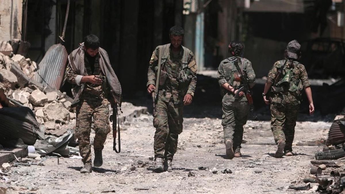 Combatientes de las Fuerzas Democráticas de Siria caminan sobre los escombros de tiendas y edificios dañados por la batalla en la ciudad de Manbij.