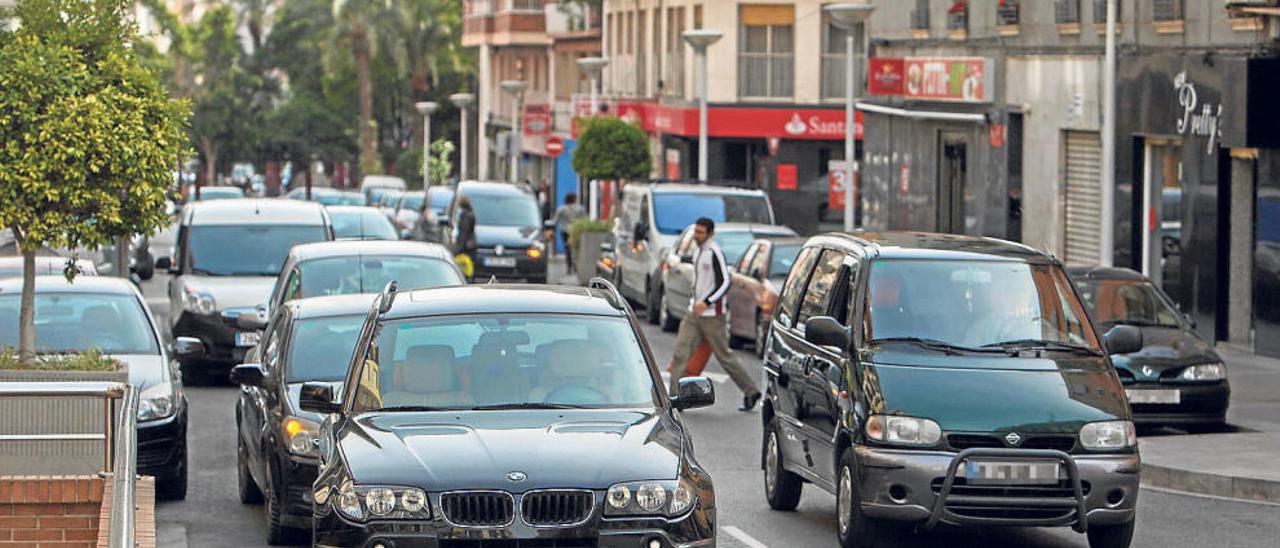 Vehículos circulando por uno de los viales del casco urbano de Elche, algunos estacionados en doble fila.