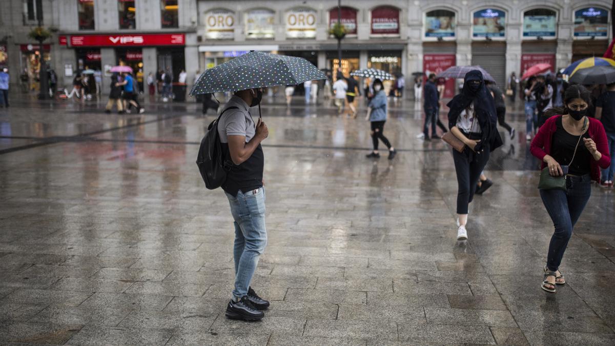 Archivo - Ciudadanos resguardándose de la lluvia durante una manifestación en la Puerta del Sol el pasado 5 de junio en Madrid