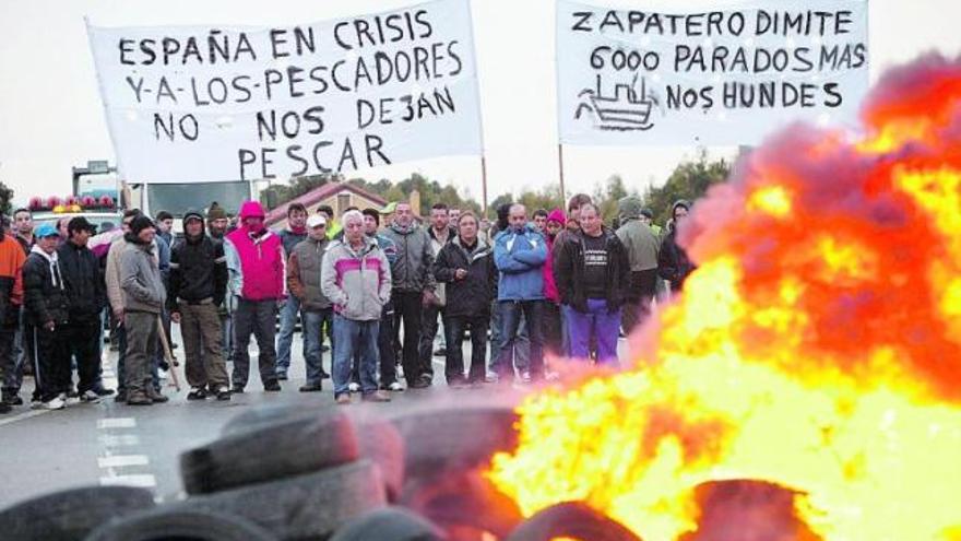 Decenas de pescadores, ayer, tras una barricada de neumáticos ardiendo en la N-632 a su paso por la localidad cudillerense de Las Dueñas.