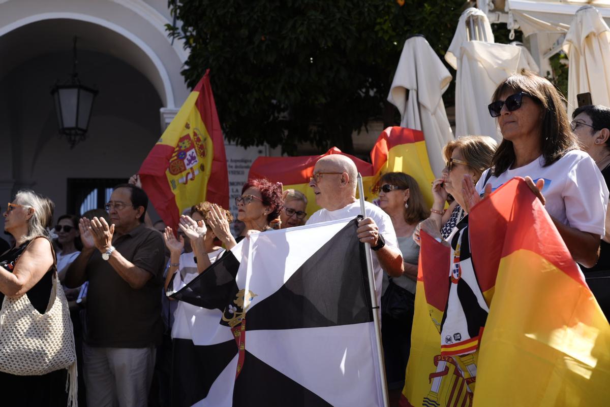Vecinos y representantes públicos se reúnen ante el Ayuntamiento de Mérida entre banderas de España y Ceuta para mostrar su respaldo a la ciudad autónoma.