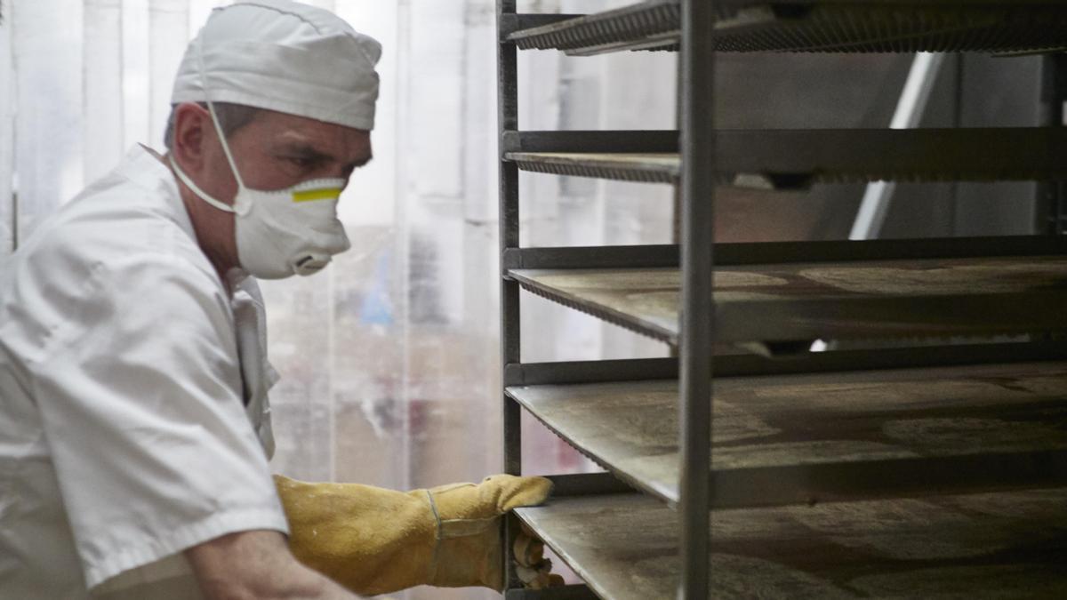 Un trabajador protegido con mascarilla maneja bandejas para cocer pan en una imagen de archivo.