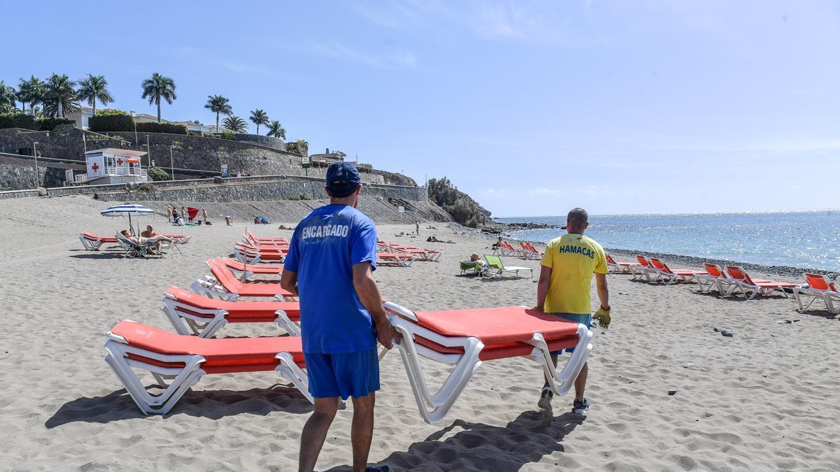Imagen de dos trabajadores colocando hamacas en la playa de Melorenas.