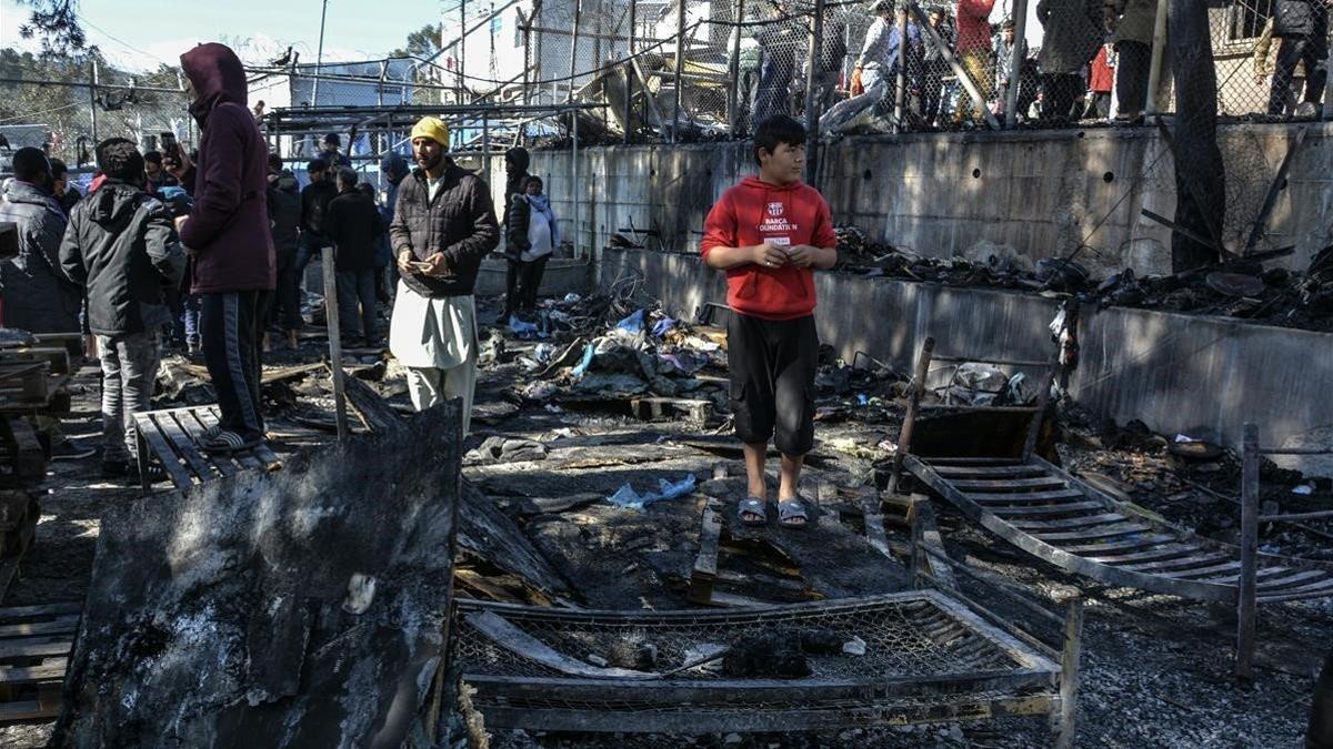 Unos migrantes permanecen junto a uno de los contenedores quemados en el incendio declarado en el campo de refugiados de Moria, en el que murió una niña.