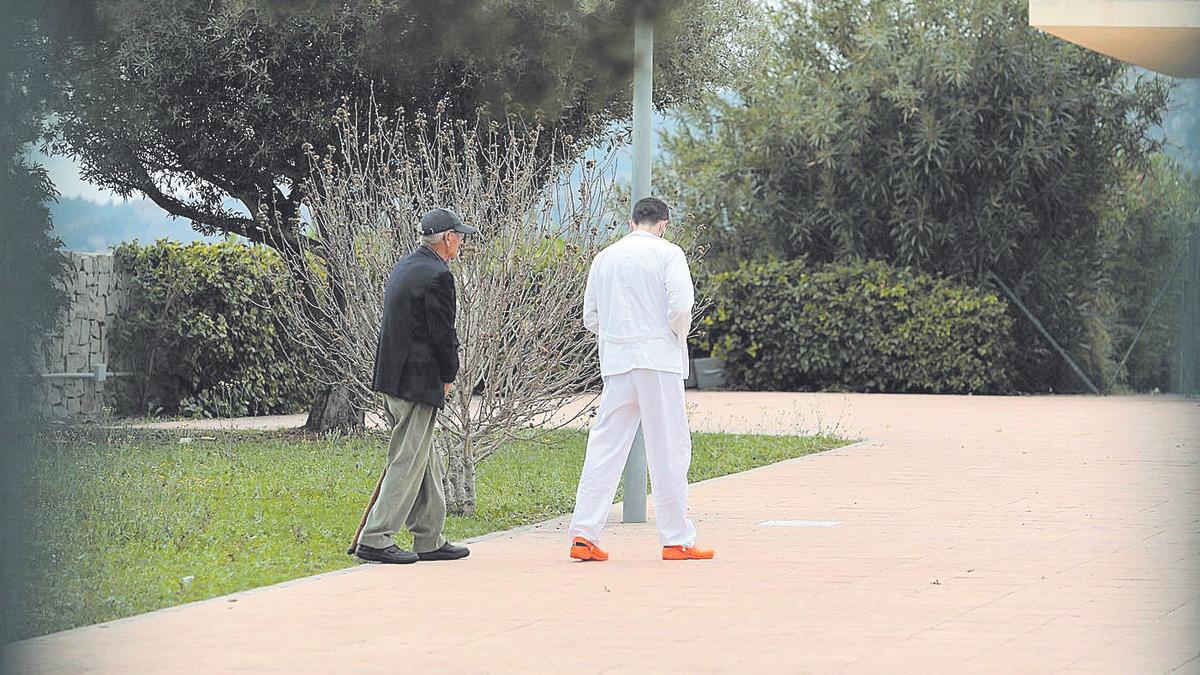 Una persona mayor pasea junto a un trabajador por los jardines de una residencia de la provincia.