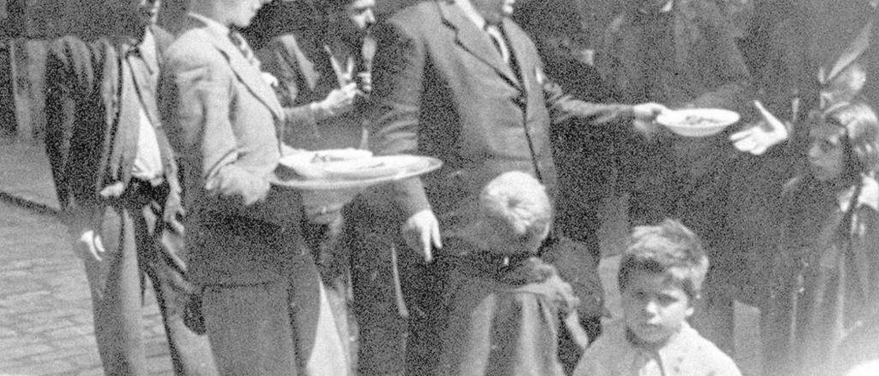 &quot;El Aldeanu&quot; entrega un plato de comida durante el reparto diario, acompañado de Luis Alfonso Gutiérrez, en 1942.