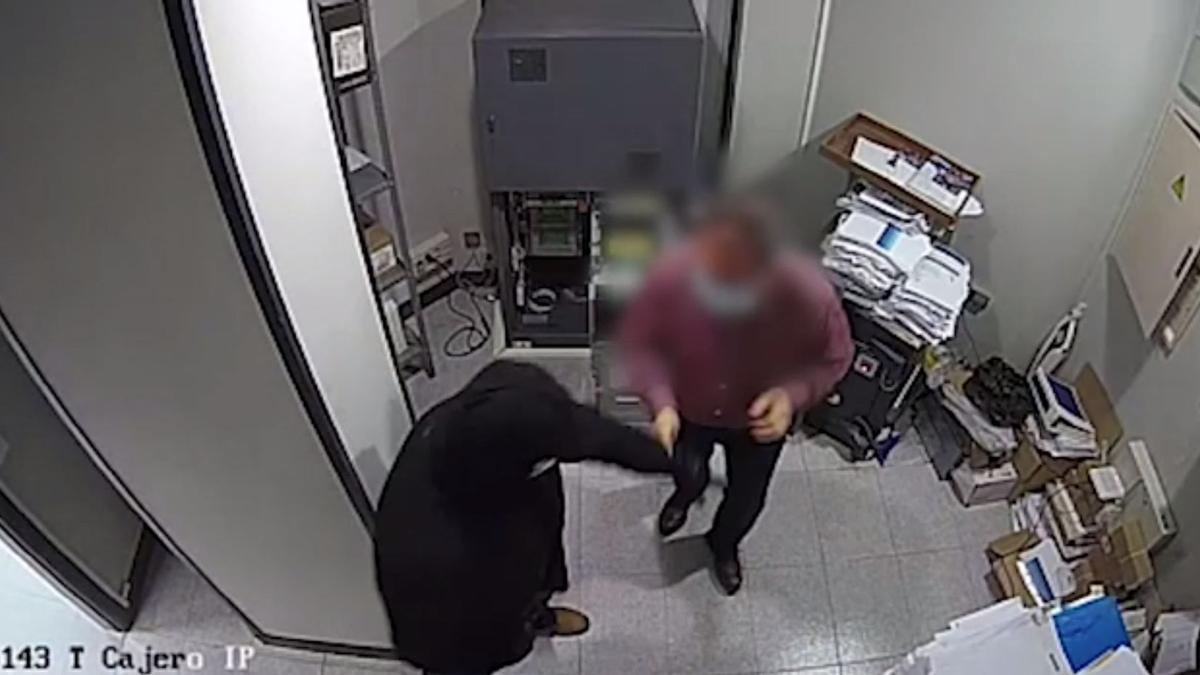 El atracador, de oscuro, arremete contra un empleado del banco en el momento de recargar el cajero.