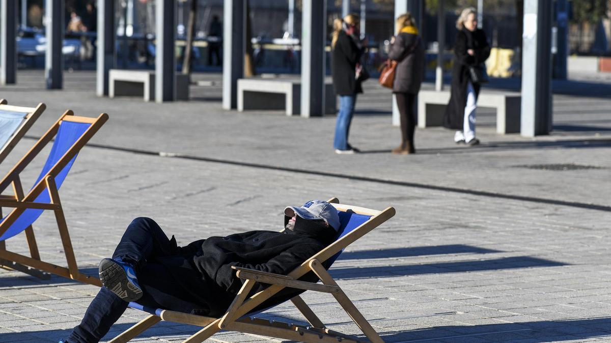 Un hombre toma el sol con abrigo en la plaza de Glories (Barcelona)