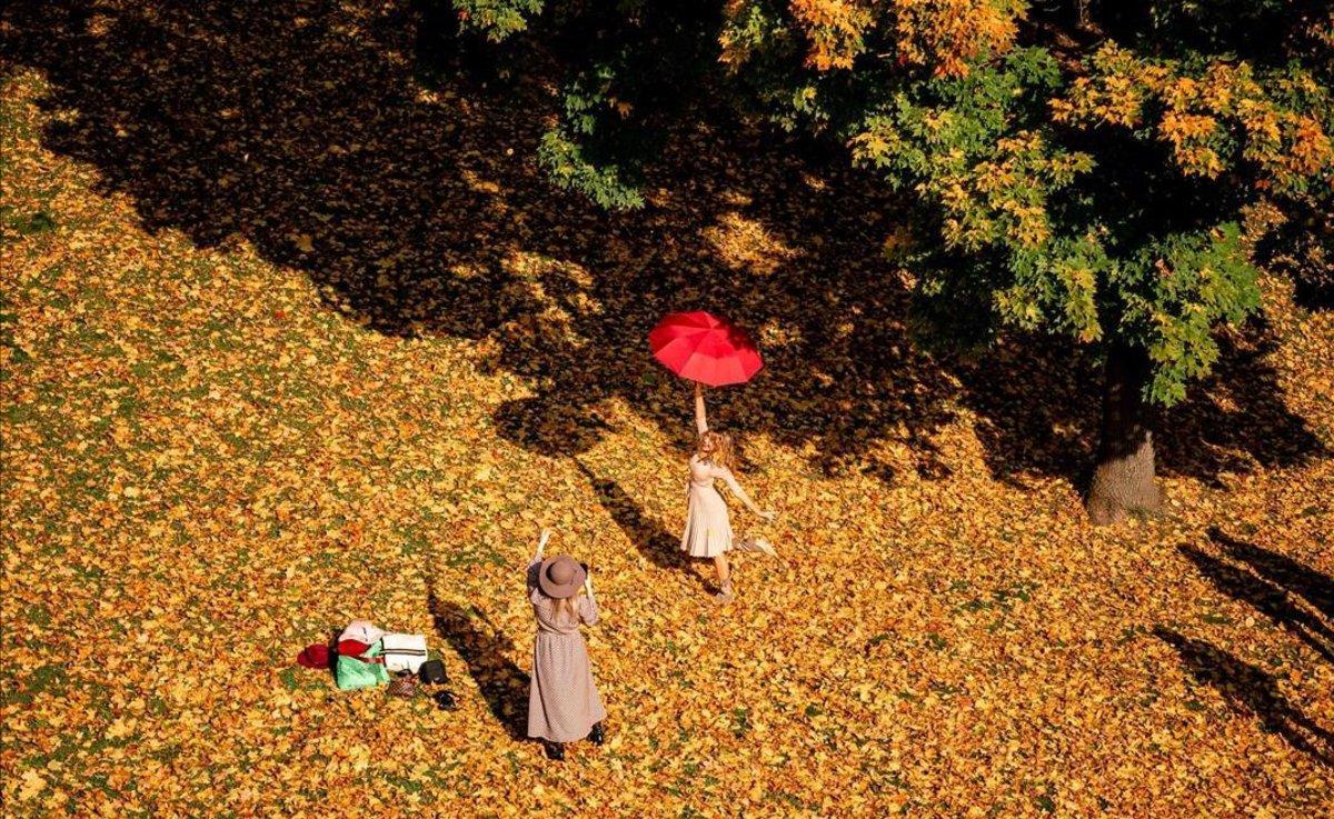 Una mujer con una sombrilla posa para una foto en un soleado día de otoño en el parque Tsaritsyno, en Moscú.   AFP)