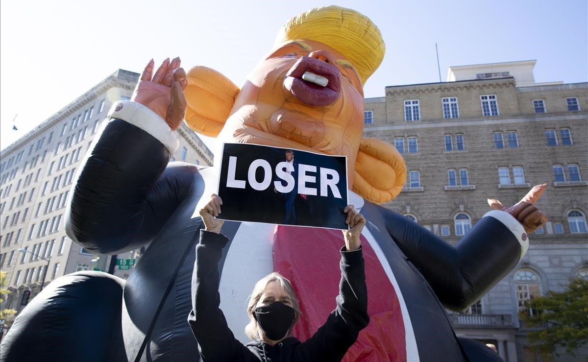 Una persona sostiene un cartel frente a una figura que representa a Trump como una rata en McPherson Square cerca de la Casa Blanca.