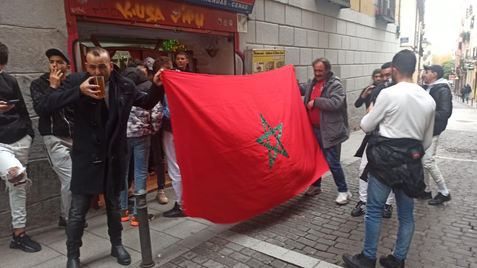 Aficionados de Marruecos sujetan una bandera de su país a las puertas del restaurante Al Bahía, en Lavapiés.