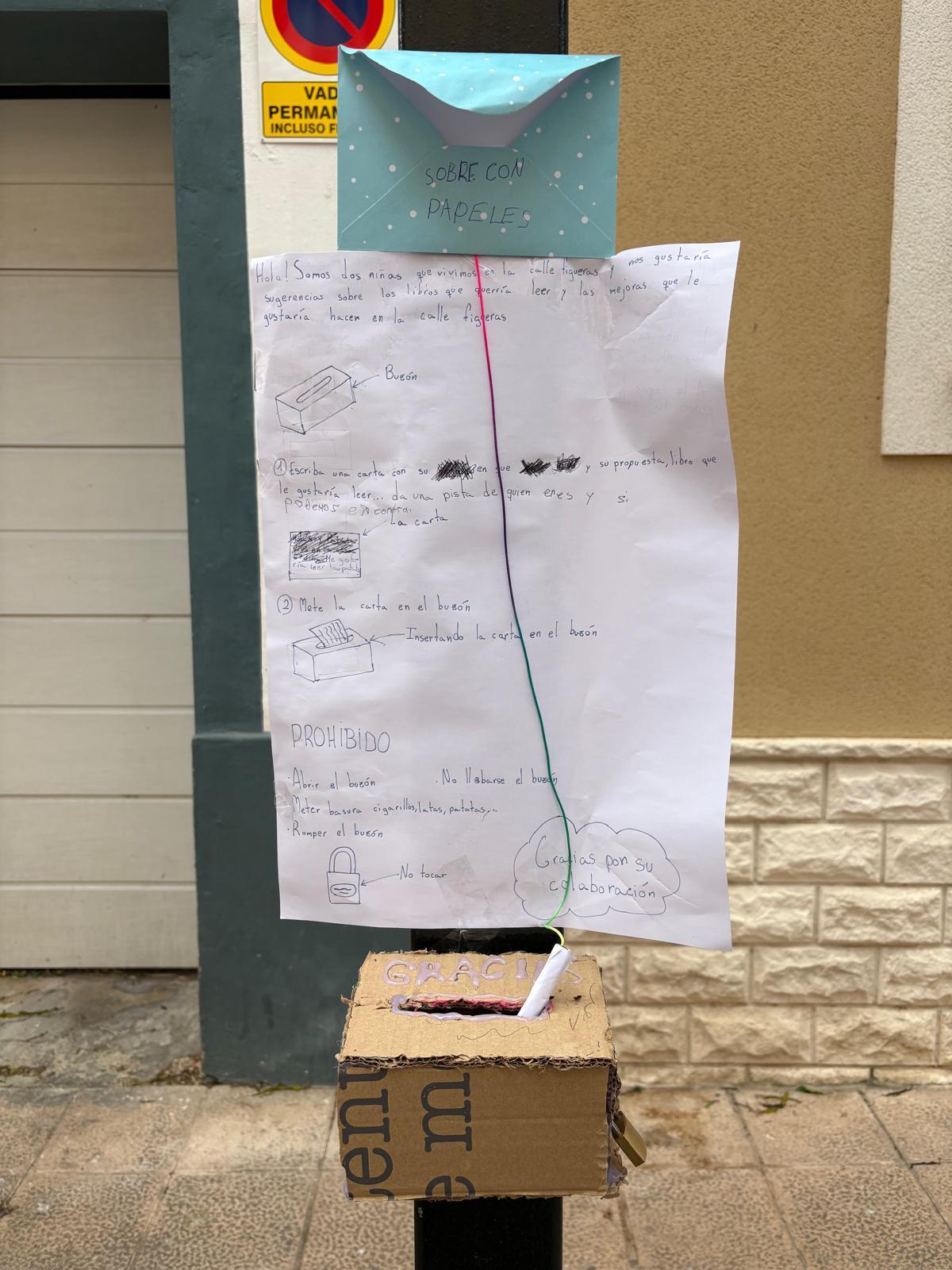 El cartel cuelga acompañado de un buzón y de un sobre con papeles para escribir.