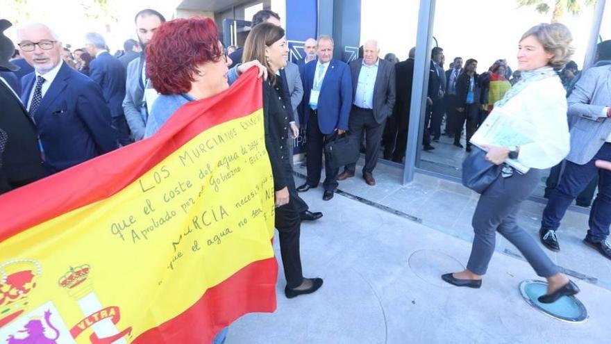 La ministra de Agricultura pasa junto a una bandera española en la que la agricultora murciana María Costa le pide que el precio del agua no exceda de los 30 céntimos el m3 y que no sea un negocio para especuladores.