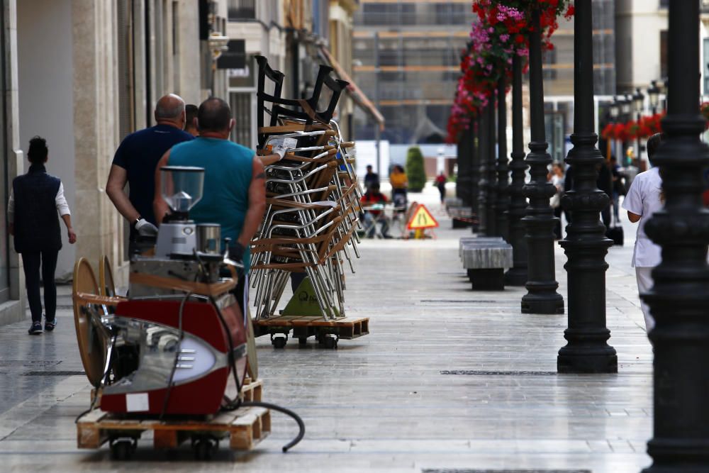 Imágenes de una lluviosa mañana de jueves en el centro de Málaga, donde al paisaje ya habitual de pocas personas y la mayoría de ellas con guantes y mascarillas se le han añadido los preparativos de bares, cafeterías y terrazas que se preparan para el inminente cambio de fase de la desescalada de la ciudad.