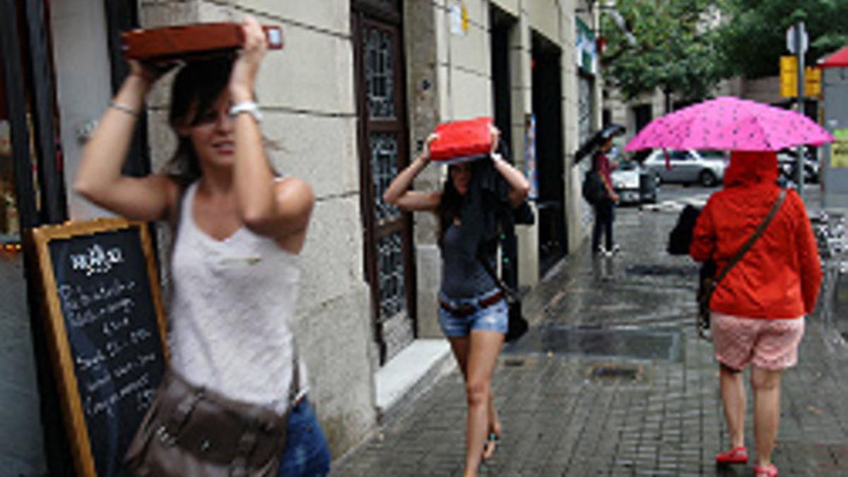 Unas chicas se guarecen de la lluvia con paraguas y libros, en Barcelona.