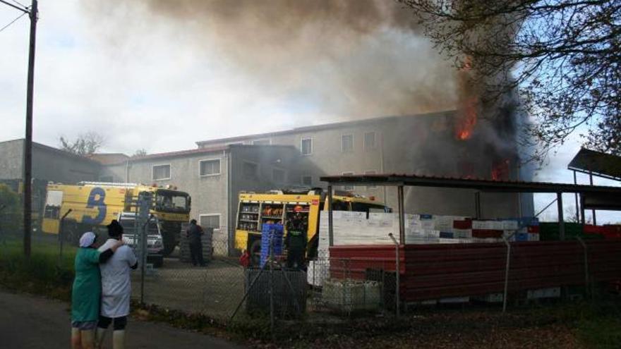 A la izquierda, empleados de la fábrica observan las labores de extinción del fuego. Arriba, un bombero trabaja  sobre uno de los camiones desplazados a Noreña, ante el edificio en llamas. | franco torre